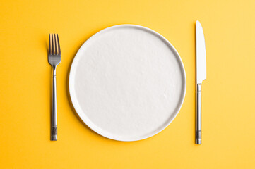 White flat empty plate with cutlery on a colored background. Top view. - obrazy, fototapety, plakaty