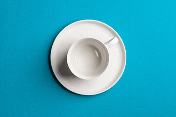 White empty cup with a saucer on a colored background. Top view.