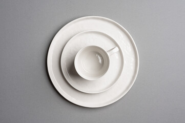 White flat empty plate and cup with a saucer on a light gray background. Top view.