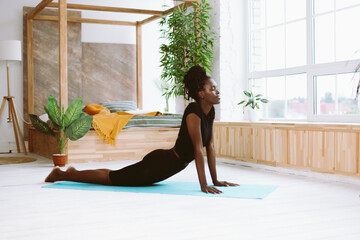 Mindful dark skin african american woman with close eyes in black outfit doing exercises, yoga on...