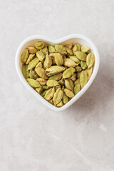 Aromatic condiment cardamom pods with seeds in white heart shape boul  on light backdrop top view with copy space
