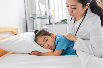 young asian doctor calming sad child lying on bed in clinic.