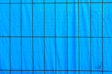 background of blue plastik foil with metal grid in foreground