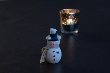 snowman ornament on black background with lit candle in background