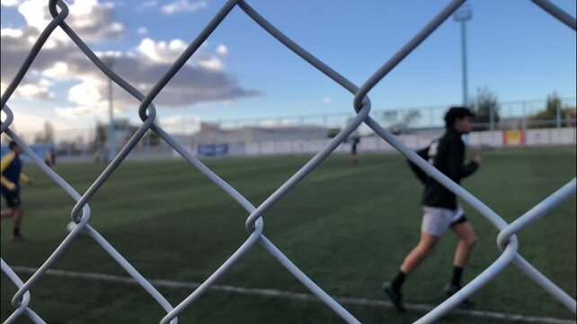 Soccer field through the  mesh that surrounds it. Boys training soccer on the field.