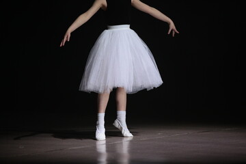 A ballet dancer in a position dancing in a white tutu and skirt on a black stage