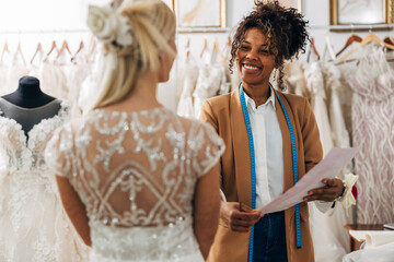 Multiracial tailor talks to a costumer in a wedding dress.