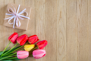 A bouquet of bright colorful tulips and a gift box on a wooden background. Copy space