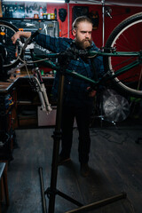 Fototapeta na wymiar Vertical portrait of repairman watching rear shifter of mountain bike, changing speeds using handlebar shift lever working in bicycle repair shop with dark interior. Concept of maintenance of bicycle.