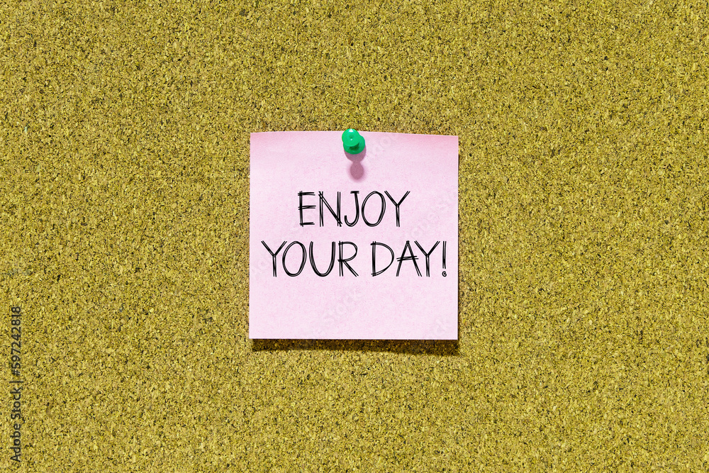 Poster enjoy your day text on pink post-it paper pinned on bulletin cork board. this message can be used in