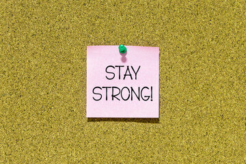Stay strong text on pink post-it paper pinned on bulletin cork board. This message can be used in...
