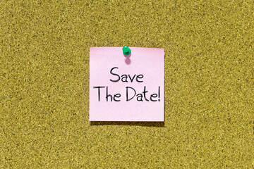 Save the date text on pink post-it paper pinned on bulletin cork board. This message can be used in...