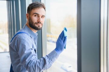 Fototapeta premium Young man cleaning window in office