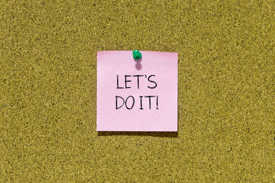 Let's do it text on pink post-it paper pinned on bulletin cork board. This message can be used in business concept about let's do it.