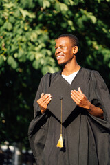 Happy african american student in mantle standing outdoors on sunny day and holding in hands...