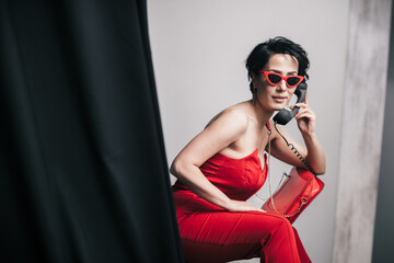 Fototapeta na wymiar Fashionable young lady in red dress talking on non-functional toy phone and holding her glamorous clutch