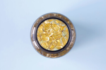 The jar with transparent yellow capsules is on a blue background. The theme of the image is health and capsules of vitamin D or omega-3. View from the top.