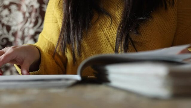 Female hands leaf through office book on table, closeup crop view. Woman read working papers, documentation. Paper work, reporting, audit, document specialist. Working lifestyle, office job.