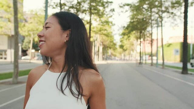 Smiling Young Woman Walking Down The Street With Mobile Phone In Her Hands, Looking Back