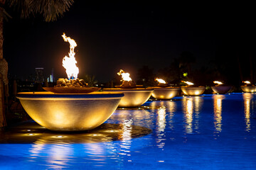 Flames of torches are reflected in the blue water of the pool against the background of the night sky