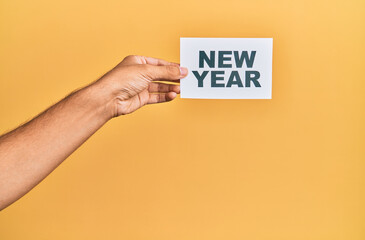 Hand of caucasian man holding paper with new year message over isolated yellow background