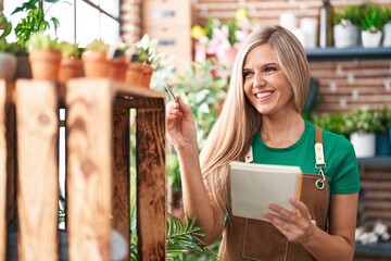 Young blonde woman florist smiling confident writing on notebook at flower shop