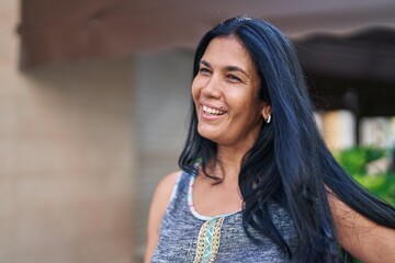 Middle age hispanic woman smiling confident looking to the side at street