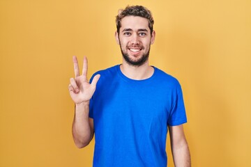 Fototapeta premium Hispanic man with beard standing over yellow background showing and pointing up with fingers number three while smiling confident and happy.