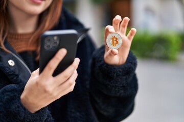 Young woman using smartphone holding bitcoin at street