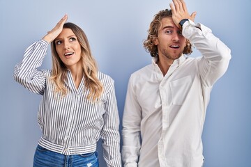 Young couple standing over blue background surprised with hand on head for mistake, remember error. forgot, bad memory concept.