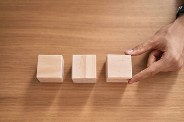 Young blond man business worker sitting on table with wooden cubes at office