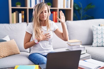 Obraz premium Young blonde woman studying using computer laptop at home swearing with hand on chest and open palm, making a loyalty promise oath