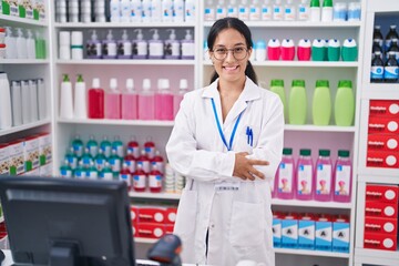 Young beautiful hispanic woman pharmacist smiling confident standing with arms crossed gesture at pharmacy