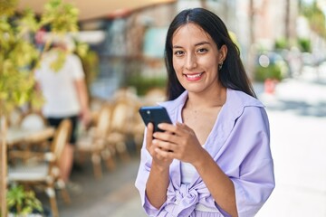 Young beautiful hispanic woman smiling confident using smartphone at street