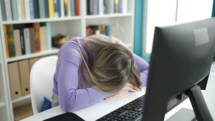 Young blonde woman student stressed with head on table at library university