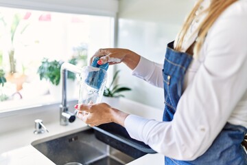 Young blonde woman washing glass at kitchen