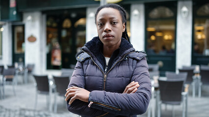 Fototapeta premium African american woman standing with serious expression and arms crossed gesture at coffee shop terrace