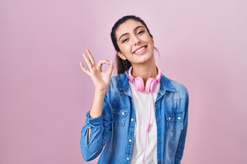 Young beautiful woman standing over pink background smiling positive doing ok sign with hand and fingers. successful expression.