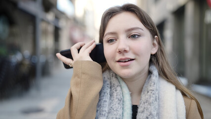 Young blonde woman smiling confident listening audio message by the smartphone at street