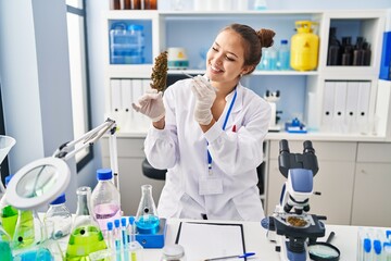 Young beautiful hispanic woman scientist holding marijuana using tweezer at laboratory