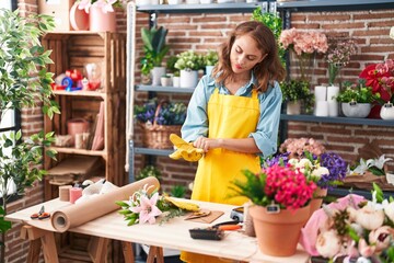 Young beautiful hispanic woman florist wearing gloves at florist