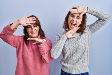 Mother and daughter standing over blue background smiling cheerful playing peek a boo with hands showing face. surprised and exited