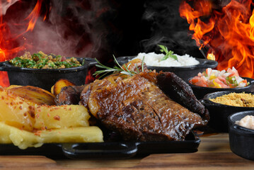 roasted meat with cassava, rice and barbecue salad on a wooden base with fire in the background