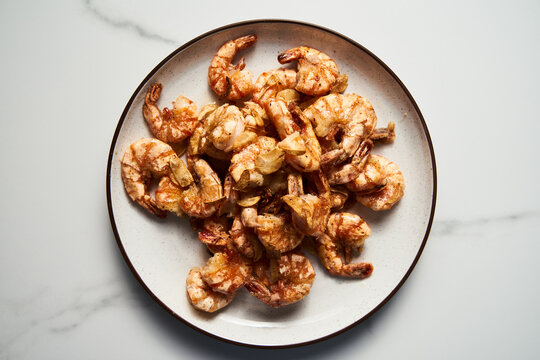 Crispy Pan fried tiger shrimps or prawns with garlic. Chinese or Asian cuisine dish. Shrimps lay on white plate on white marble background. Top view food photo.