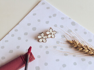 Composition with female accessories. A pair of small flower  earrings, lipstick and a ear of wheat on polka dot background. Vintage fashion concept and minimalist style. Spring mockup. Top view.