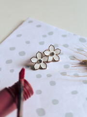 Composition with female accessories. A pair of small flower  earrings and a lipstick on polka dot background. Vintage fashion concept and minimalist style. Spring mockup. Top view.