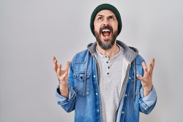 Young hispanic man with tattoos wearing wool cap crazy and mad shouting and yelling with aggressive...