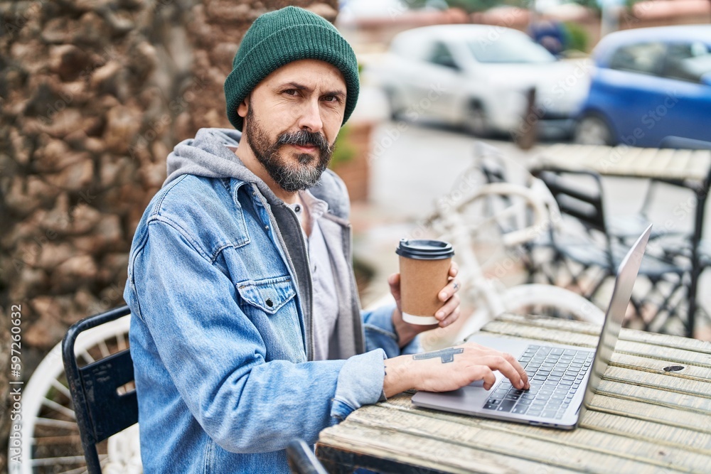 Poster young bald man using laptop drinking coffee at coffee shop terrace