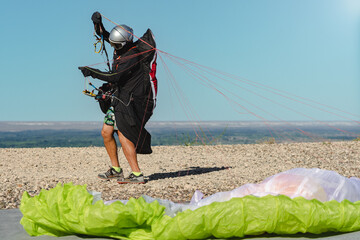 Paraglider on his suit at the top of a hill taking ropes for flying
