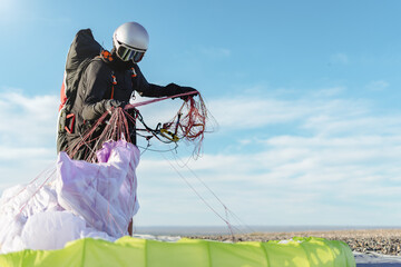 Professional paraglider taking ropes from the floor after flight on a sunny day